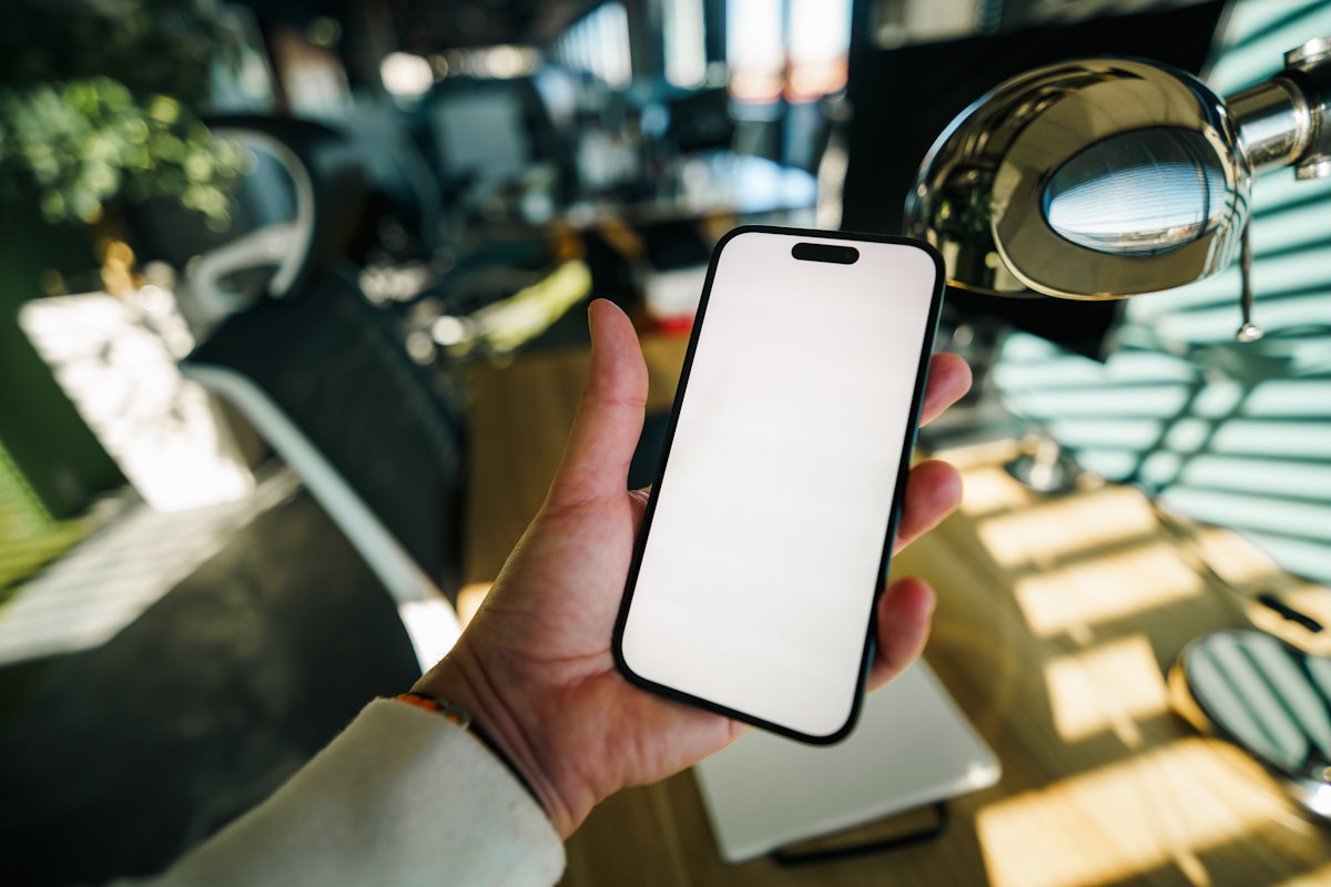 Hand holding a smartphone with a blank white screen.