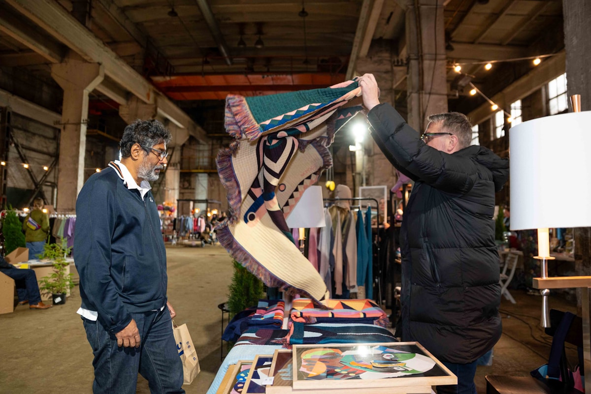 Two men examine a patterned textile at a market stall.